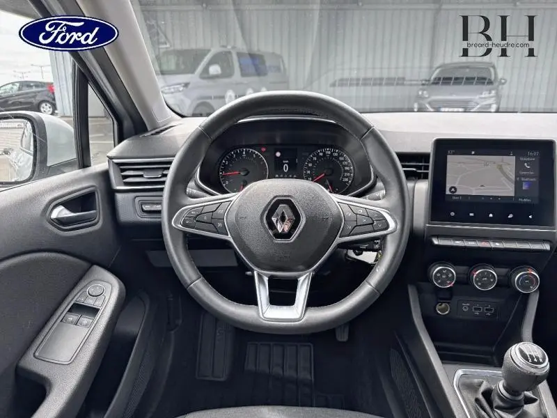 Vue intérieure centrée sur le volant Renault avec tableau de bord, écran tactile et levier de vitesses manuel.