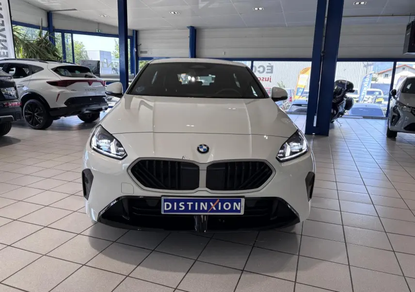 Vue avant d'une BMW Série 1 120d blanche 2025 en finition M Sport, avec calandre noire et phares allumés.