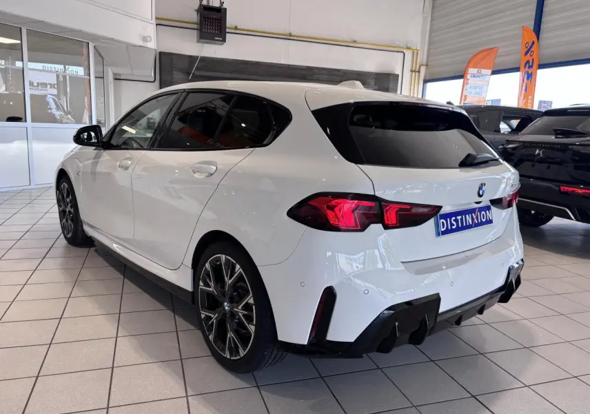 BMW Série 1 120d M Sport blanc vue 3/4 arrière droit en intérieur, avec jantes noires et détails sportifs.