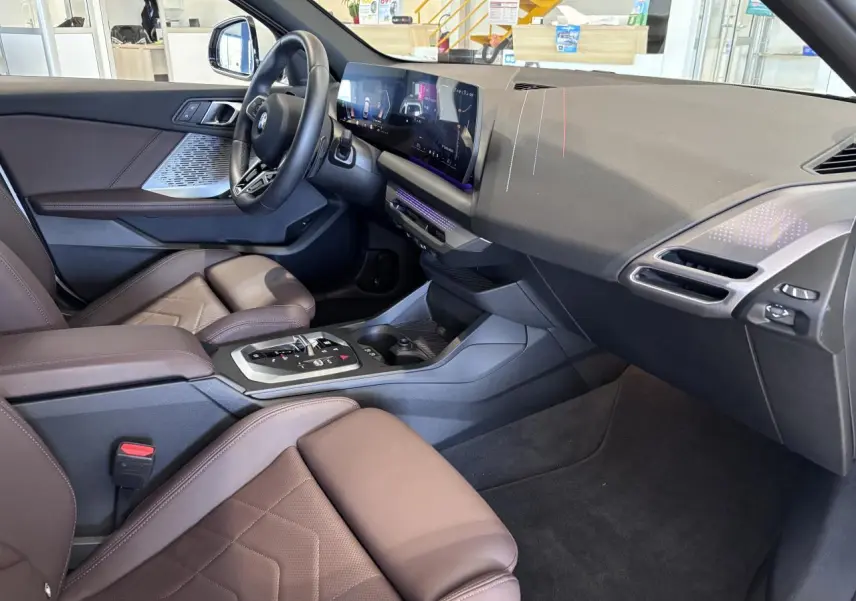 Vue intérieure côté passager de la BMW Série 1 120d M Sport 2025, sièges marron et tableau de bord moderne noir.