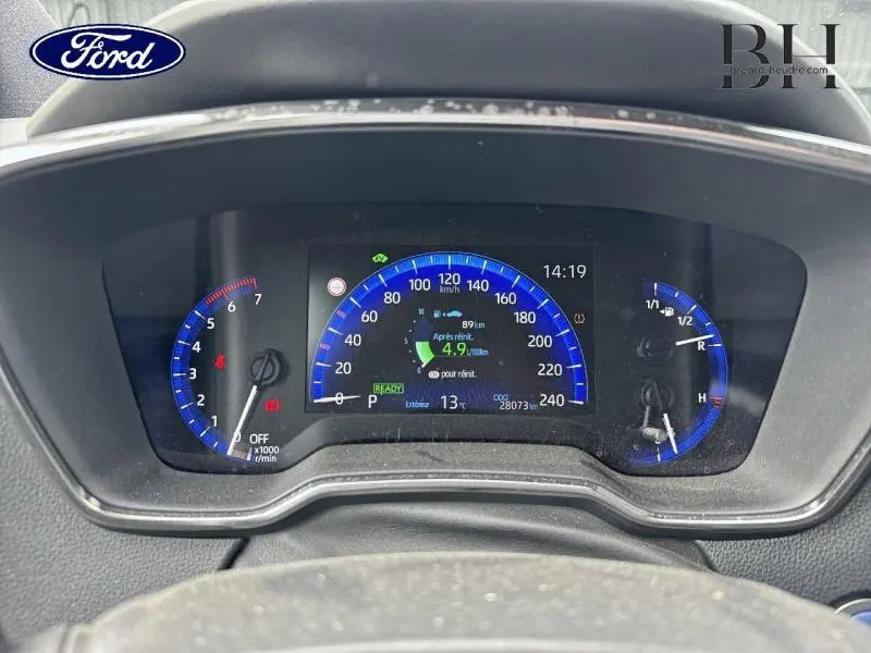 Vue rapprochée du tableau de bord numérique de la Toyota Corolla 122h Dynamic Business avec affichage bleu et informations de conduite.