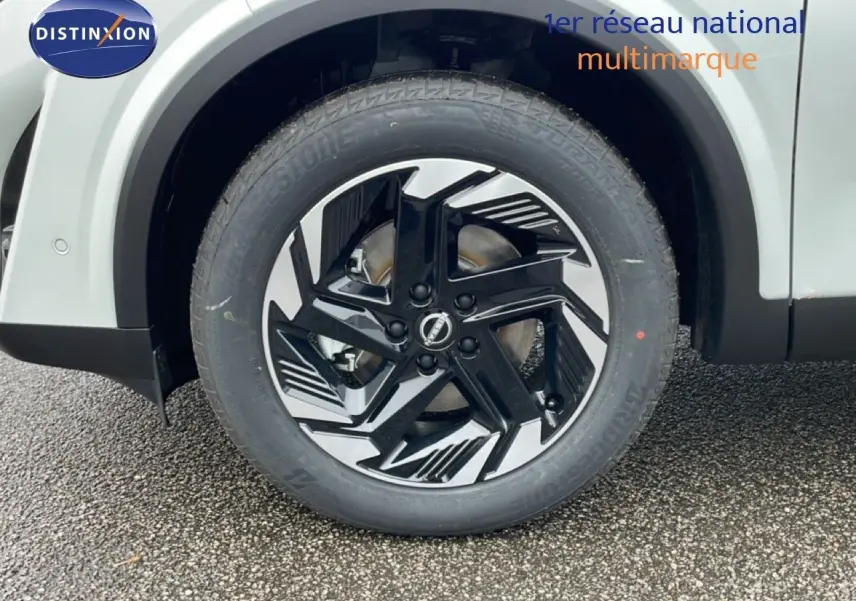 Gros plan sur la roue avant droite du Nissan Qashqai blanc nacré avec jante alliage noire et argentée au design moderne.