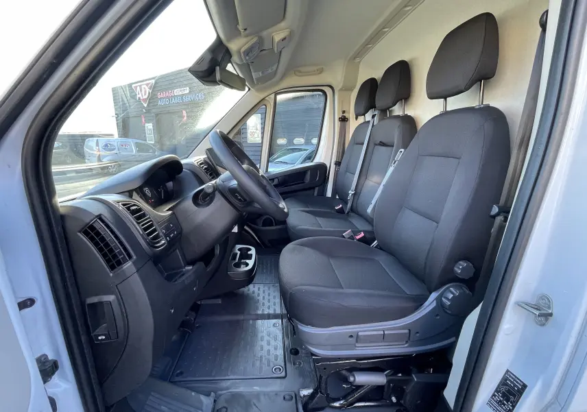 Vue intérieure côté conducteur du Peugeot Boxer Fourgon blanc 2025, montrant les trois sièges noirs et le tableau de bord.