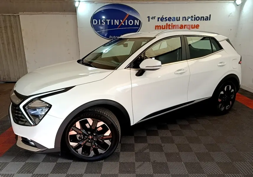 Vue 3/4 avant droit d'un KIA Sportage blanc 2022 hybride rechargeable, avec jantes noires et feux LED distinctifs.