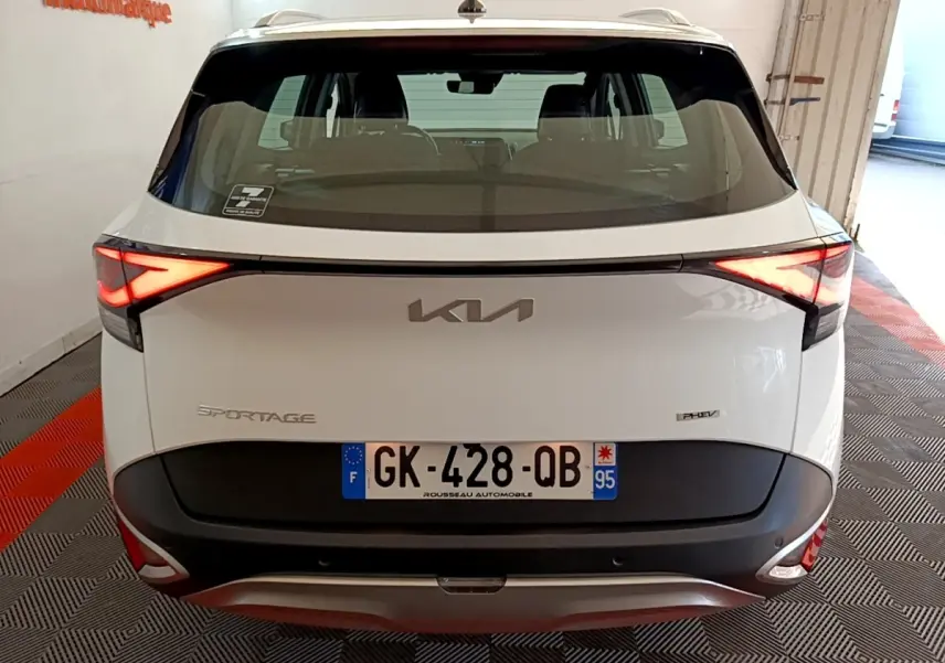 Vue arrière d'un KIA Sportage blanc hybride rechargeable avec feux LED allumés et plaque d'immatriculation française.