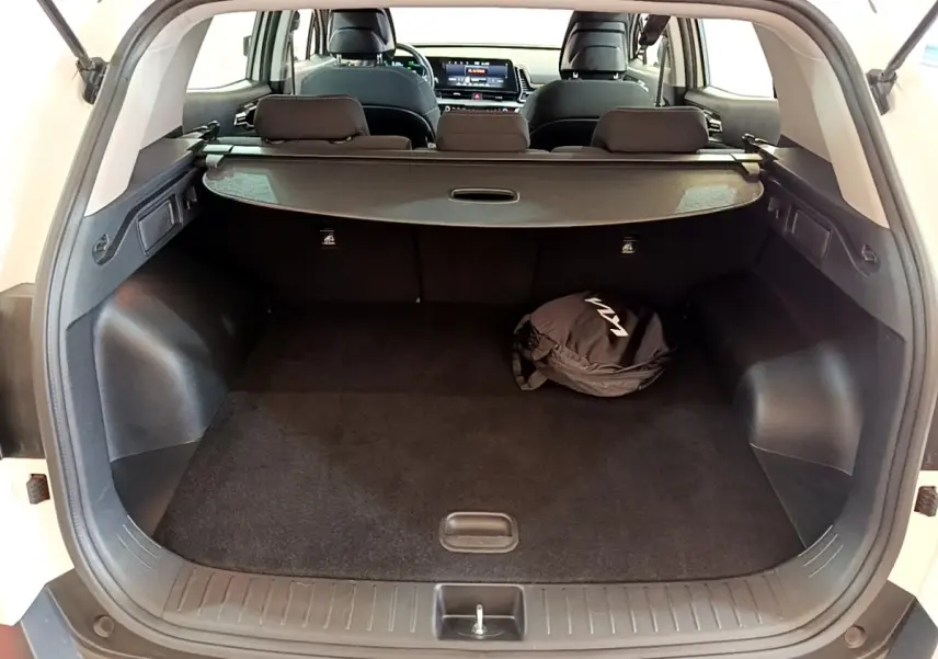 Vue arrière du coffre ouvert du KIA SPORTAGE blanc, avec cache-bagages et sac noir marqué KIA visible à l'intérieur.