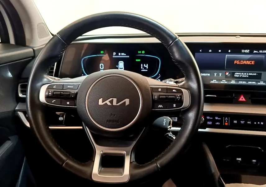 Vue intérieure centrée sur le volant cuir KIA et le tableau de bord numérique avec écran tactile du Kia Sportage blanc 2022.
