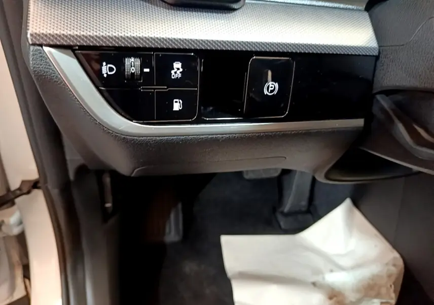 Détail intérieur côté conducteur du Kia Sportage blanc 2022 montrant les commandes d’éclairage et frein à main électrique.
