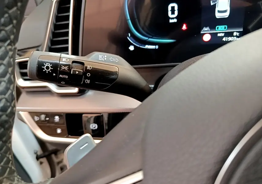 Gros plan sur la manette des feux et le tableau de bord numérique du Kia Sportage blanc, affichage digital visible.