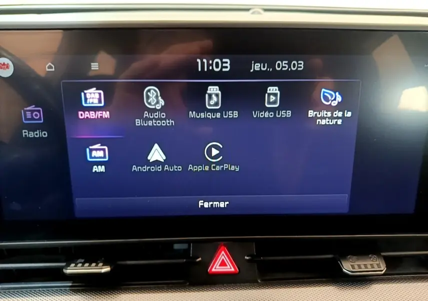 Écran tactile central du tableau de bord du Kia Sportage blanc, affichant les options multimédias et connectivité.
