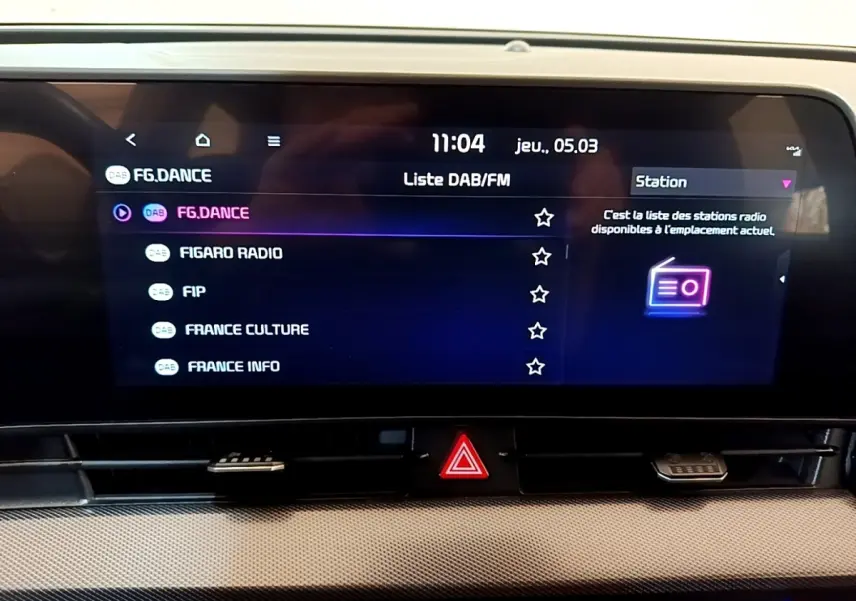 Écran tactile central du tableau de bord du Kia Sportage blanc, affichant la liste des stations radio DAB/FM.
