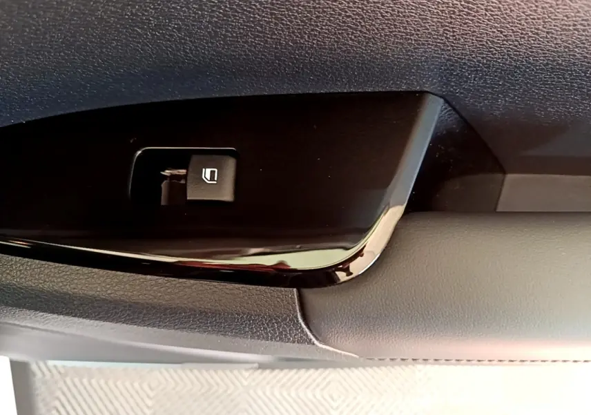 Gros plan sur le bouton de commande de la vitre électrique côté conducteur, intérieur noir et gris du Kia Sportage blanc.