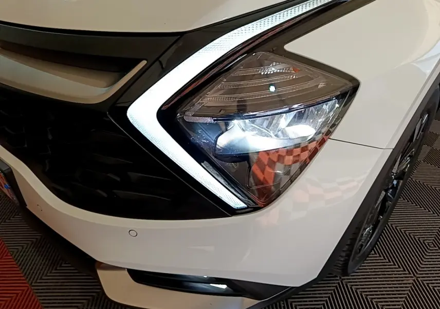 Gros plan sur le phare avant droit blanc du KIA SPORTAGE 2022 avec éclairage LED et calandre noire.