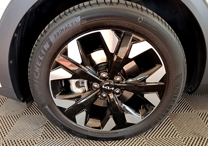 Gros plan sur la roue avant droite du KIA SPORTAGE blanc, jante alliage noir brillant avec logo KIA central.