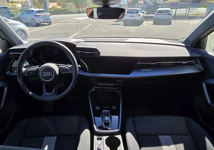 Vue intérieure avant de l'Audi A3 Sportback 2024 avec tableau de bord noir et volant multifonctions cuir.