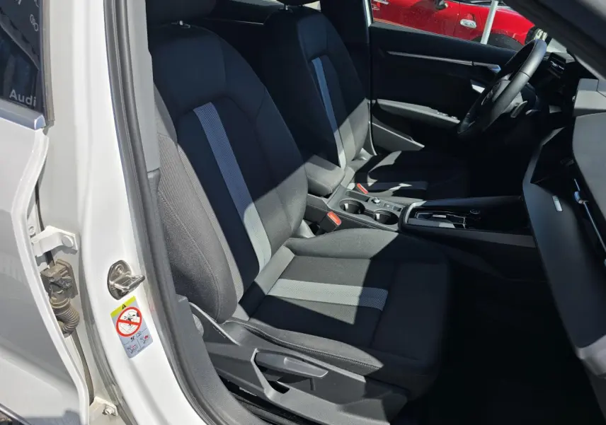Vue intérieure côté conducteur de l'Audi A3 Sportback 2024 blanc Arkona, sièges tissu noir avec bande grise centrale.