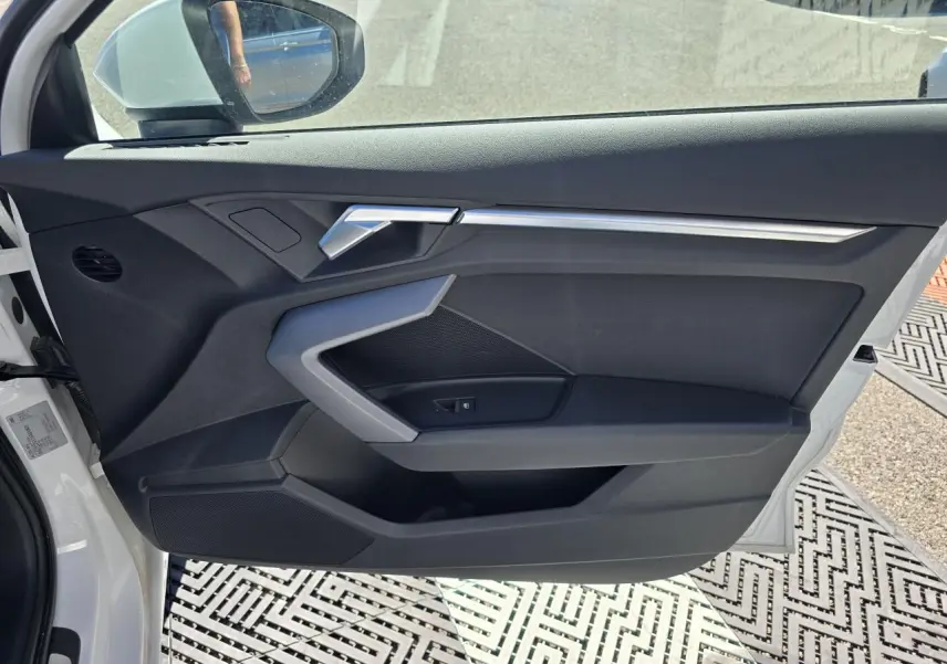 Vue intérieure côté gauche de la porte avant d’une Audi A3 Sportback blanche avec garniture noire et insert argenté.
