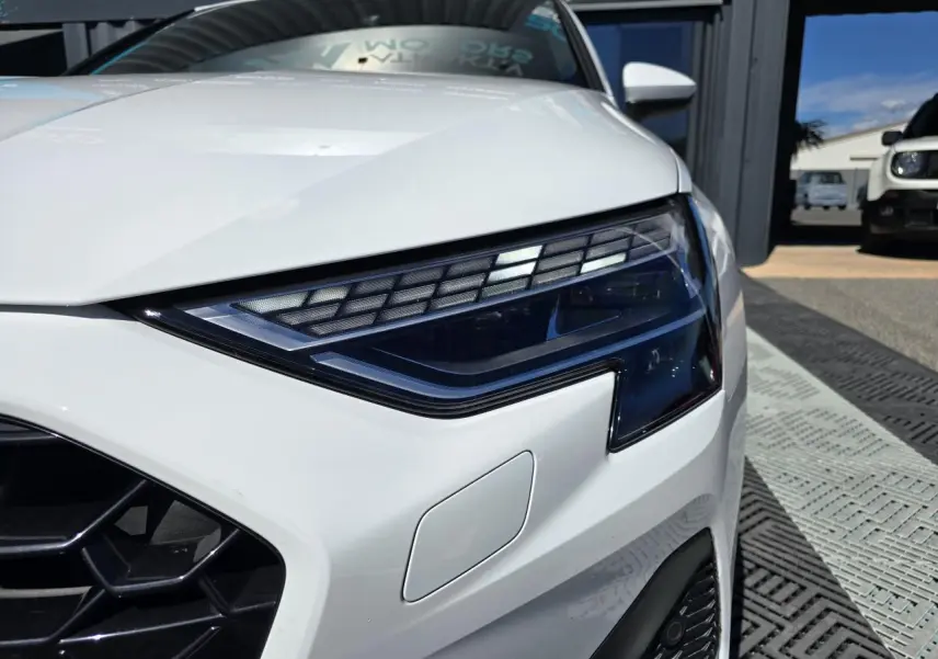 Gros plan sur le phare avant droit blanc Arkona d’une Audi A3 Sportback 2024 avec calandre noire et détails LED.