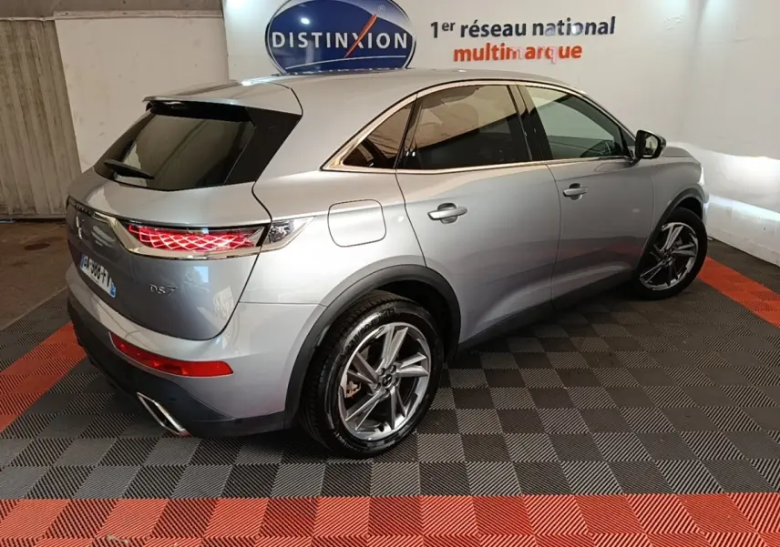 Vue 3/4 arrière droite du DS7 Crossback E-TENSE 225 Business gris foncé avec feux arrière LED allumés en intérieur showroom.
