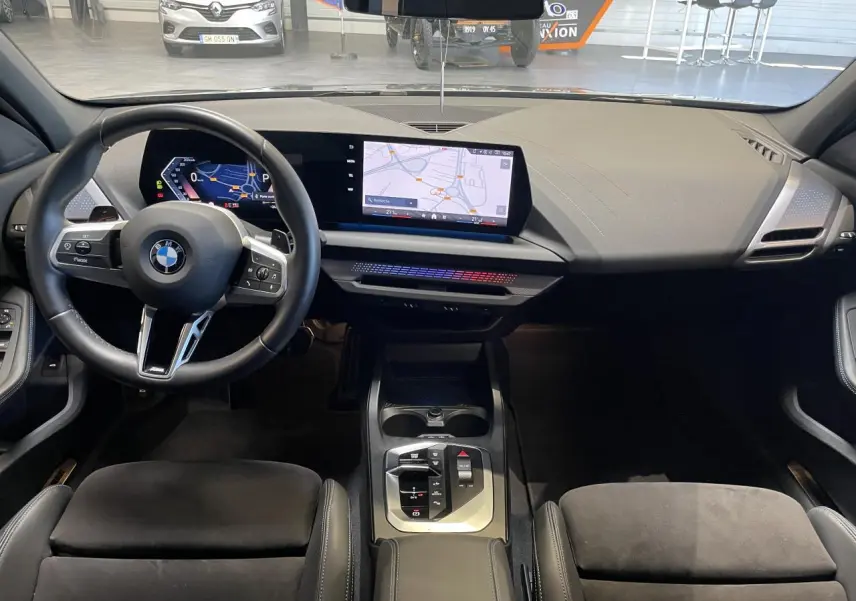 Vue intérieure avant de la BMW Série 1 120d M Sport 2025, tableau de bord moderne avec écran large et volant cuir noir.