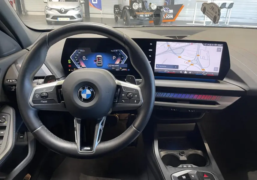 Vue intérieure centrée sur le volant cuir M et le BMW Curved Display avec navigation, ambiance lumineuse M Sport visible.