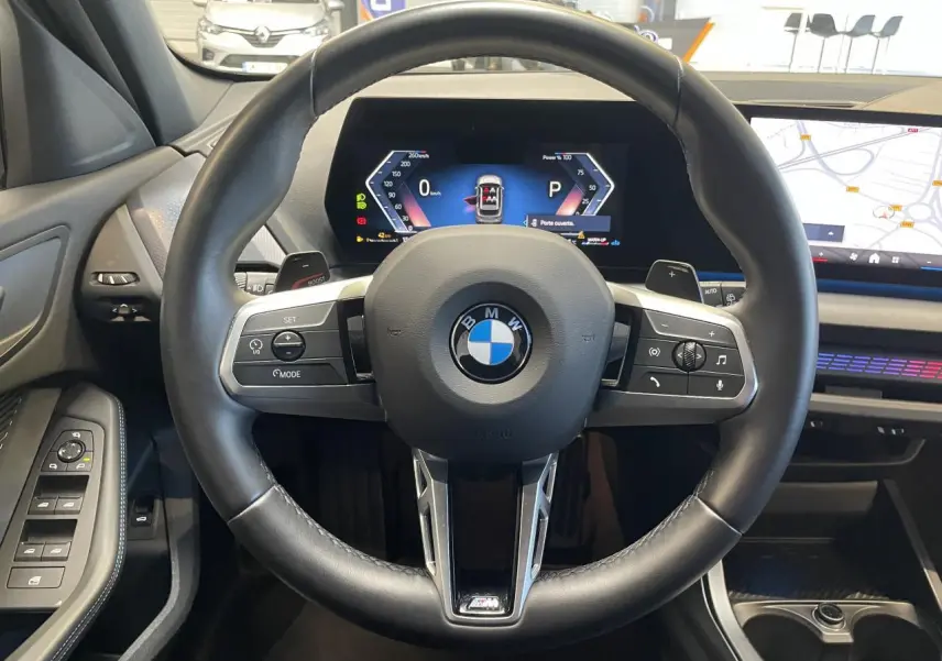 Vue intérieure centrée sur le volant cuir noir M Sport et le tableau de bord numérique de la BMW Série 1 120d gris.