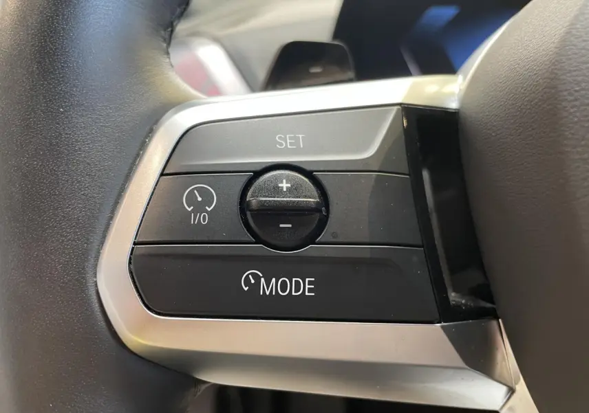 Gros plan sur les commandes de régulateur de vitesse au volant cuir noir de la BMW Série 1 120d M Sport 2025.