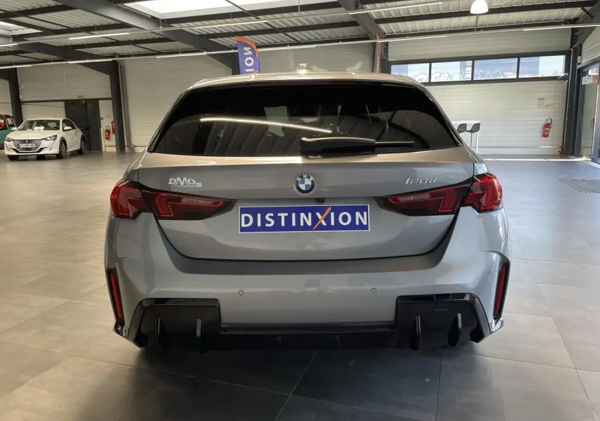 Vue arrière d'une BMW Série 1 120d gris avec diffuseur noir et feux LED en intérieur showroom.