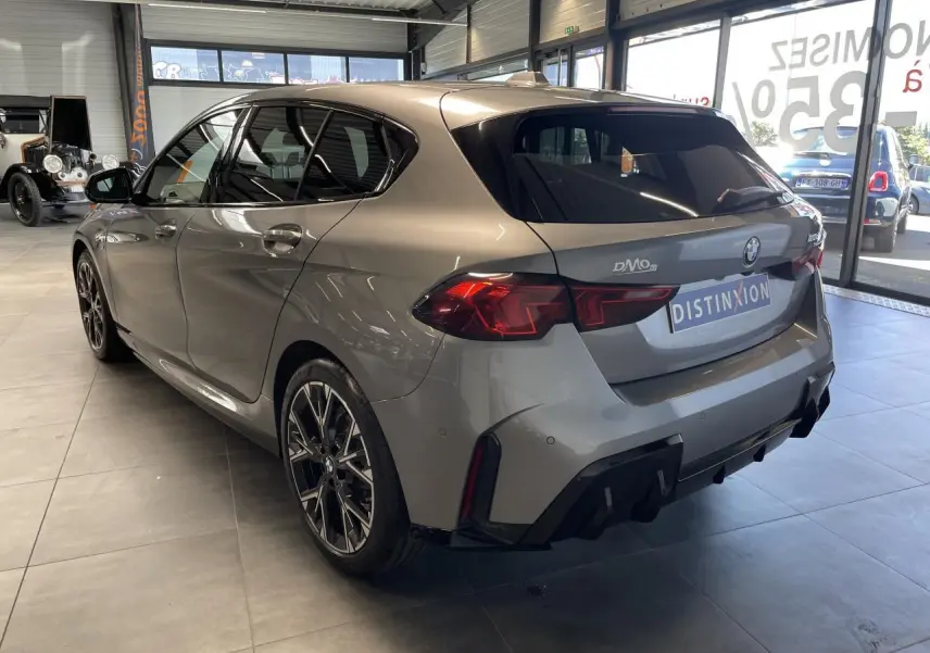 BMW Série 1 120d M Sport gris vue 3/4 arrière droit en intérieur avec jantes bicolores et diffuseur noir M Sport.