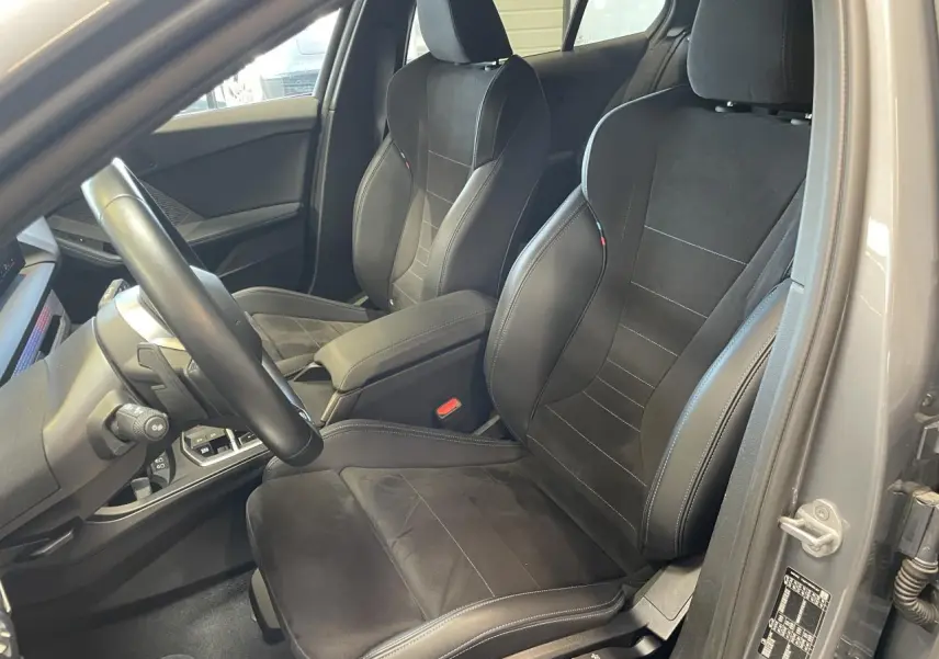 Vue intérieure côté conducteur de la BMW Série 1 120d M Sport 2025 avec sièges sport Alcantara noirs et surpiqûres bleues.