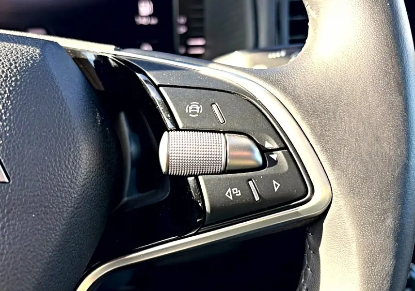 Gros plan sur les commandes noires et argentées du volant cuir du Skoda Karoq gris, côté gauche.