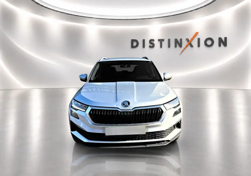 Vue frontale d'un Skoda Karoq gris 2025 avec calandre noire et signature lumineuse LED, dans un showroom épuré.