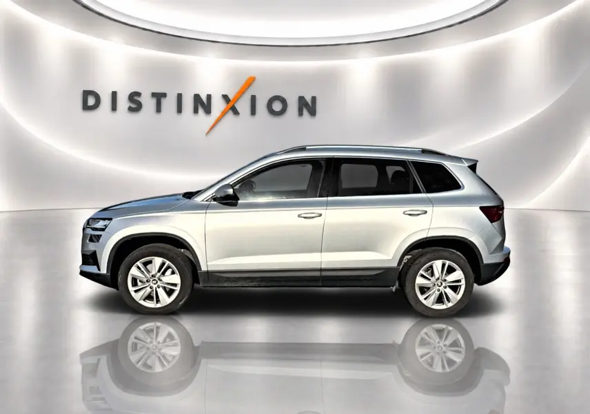 Profil droit d'un Skoda Karoq gris 2025 dans un showroom lumineux avec logo Distinxion en arrière-plan.