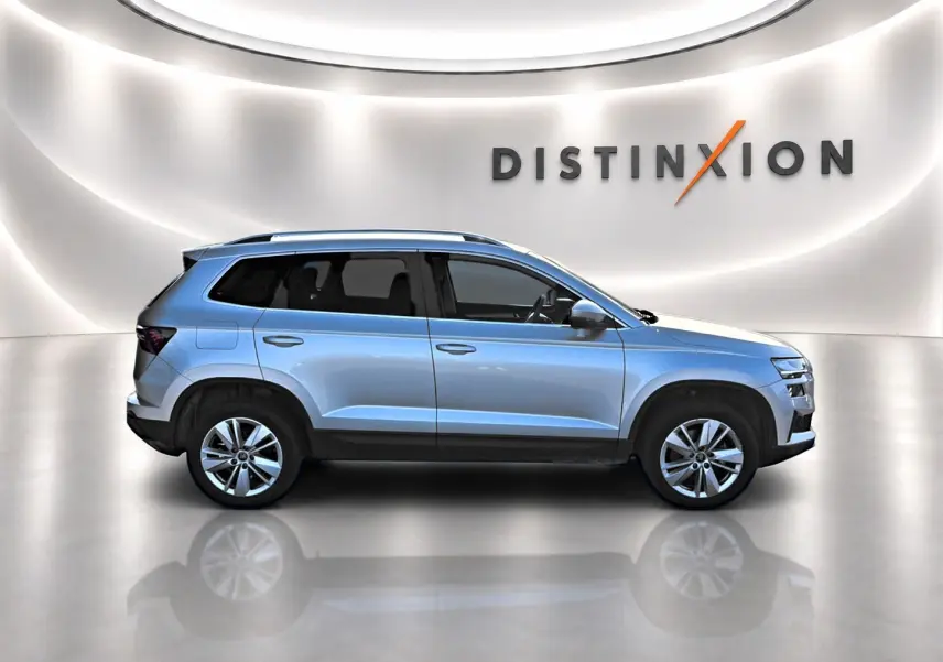 Vue de profil droit du SUV SKODA KAROQ gris clair avec barres de toit et jantes alliage, dans un showroom lumineux.