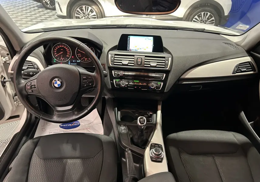 Vue intérieure de la BMW Série 1 116d Business 2015, tableau de bord noir avec écran central et boîte manuelle.