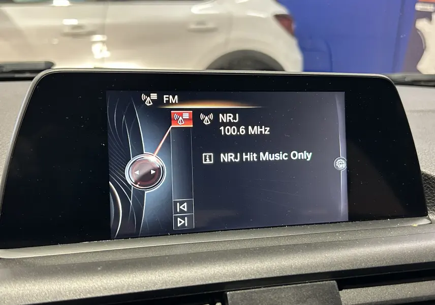 Écran central de la BMW Série 1 116d Business 2015 affichant la radio FM NRJ à 100.6 MHz, intérieur noir.