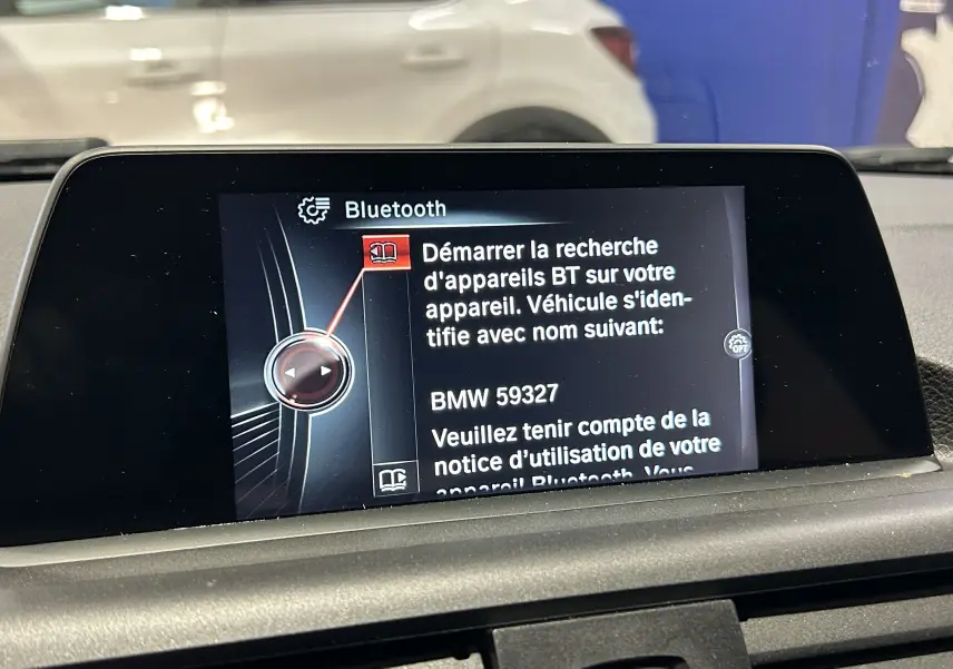 Affichage de l'écran central du système Bluetooth dans une BMW Série 1 blanche, vue intérieure du tableau de bord.