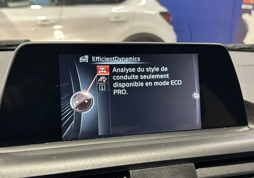 Vue intérieure centrée sur l'écran multimédia de la BMW Série 1 blanche, avec affichage du mode EfficientDynamics.