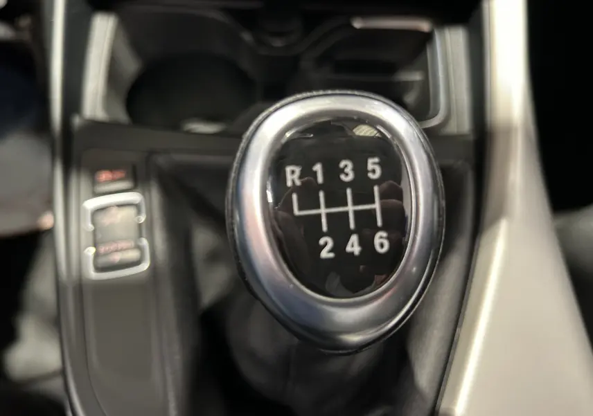 Gros plan sur le levier de vitesses manuel d'une BMW Série 1 116d blanche, montrant la grille à 6 rapports et la marche arrière.