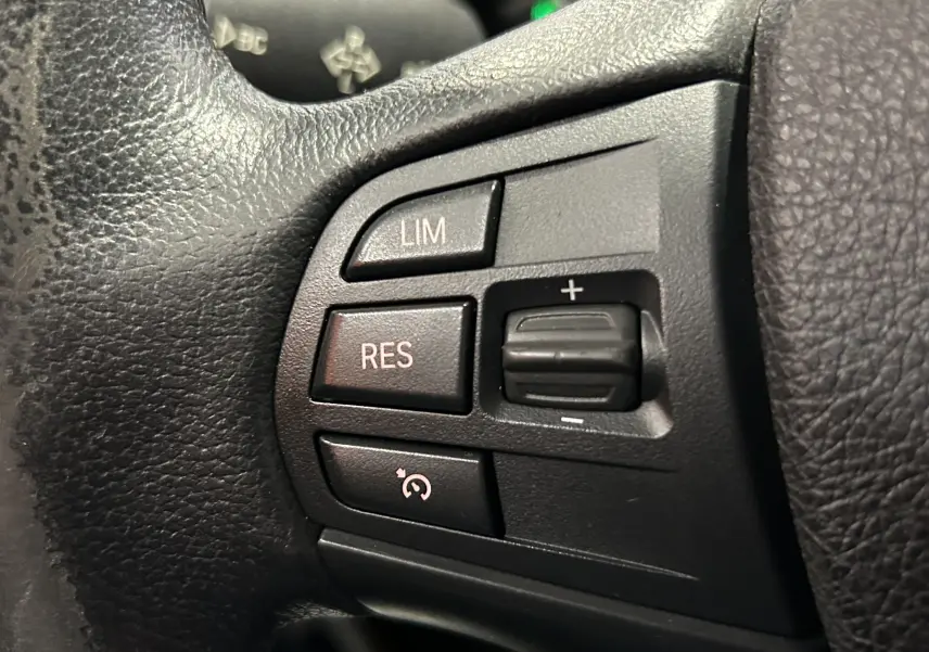 Gros plan sur les boutons de commande du régulateur de vitesse au volant en cuir noir d'une BMW Série 1 blanche 116d Business 2015.