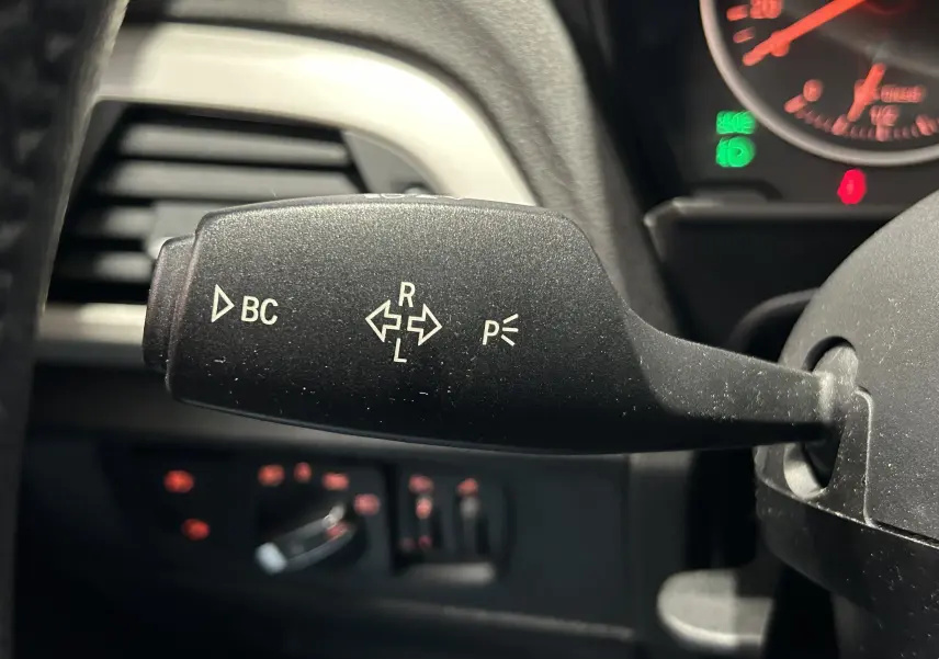 Gros plan sur la commande de clignotant noire à gauche du volant dans l’habitacle d’une BMW Série 1 blanche.