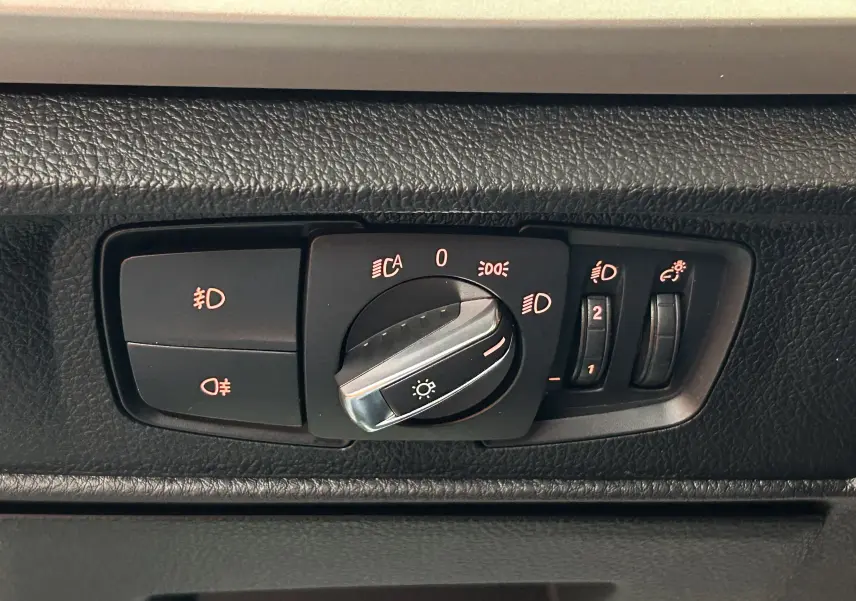 Gros plan sur le bouton de commande des phares intérieur d'une BMW Série 1 blanche, modèle 116d Business 2015.
