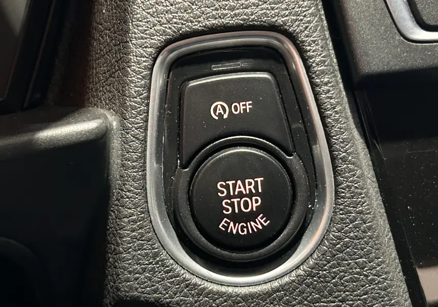 Gros plan sur le bouton Start Stop Engine noir entouré de plastique texturé dans une BMW Série 1 blanche de 2015.