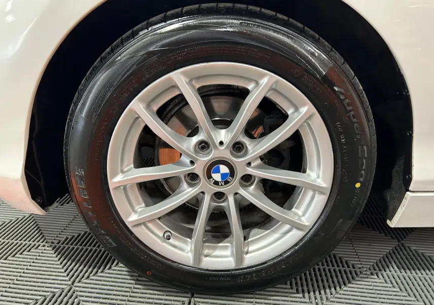 Gros plan sur la roue avant droite d'une BMW Série 1 blanche, mettant en valeur la jante alliage et le pneu neuf.