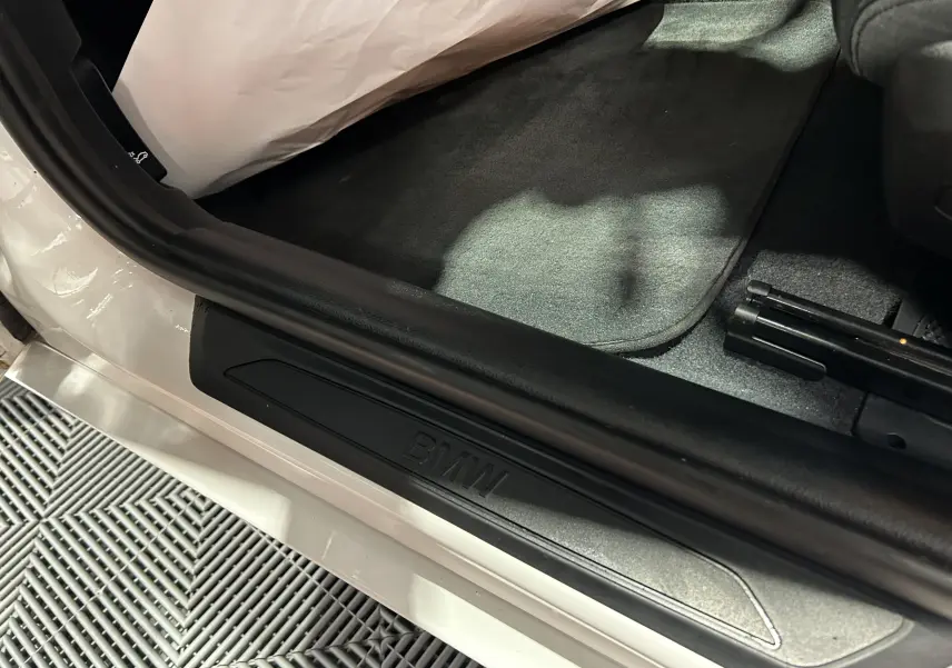 Gros plan sur le seuil de porte côté conducteur d'une BMW Série 1 blanche avec logo BMW en relief.