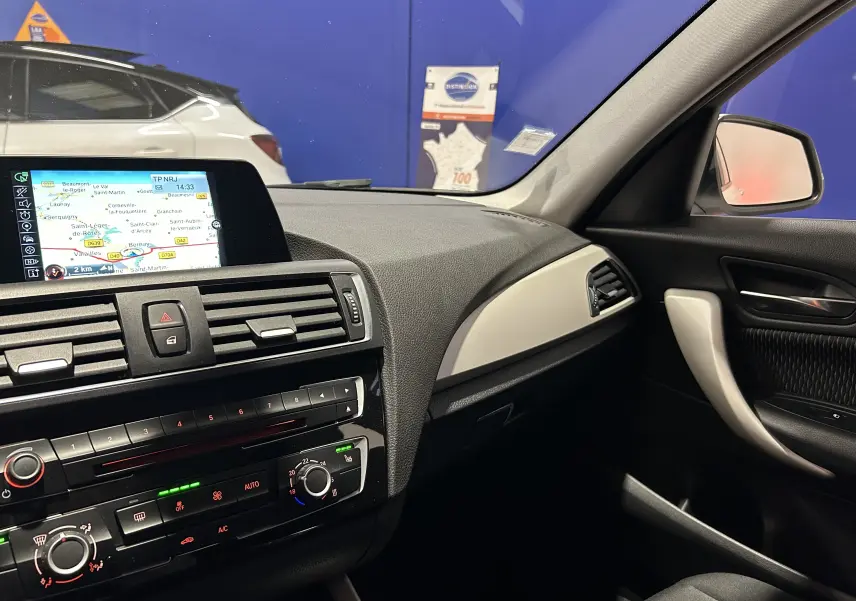 Vue intérieure côté passager de la BMW Série 1 blanche, avec tableau de bord et écran de navigation allumé.
