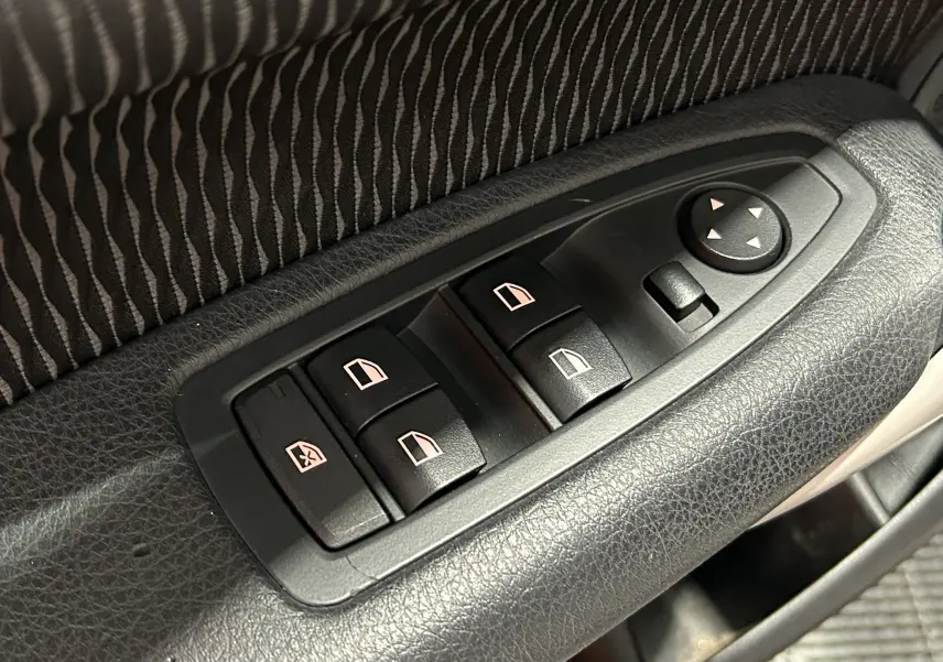 Gros plan sur les commandes de lève-vitres et réglage des rétroviseurs côté conducteur d'une BMW Série 1 blanche.
