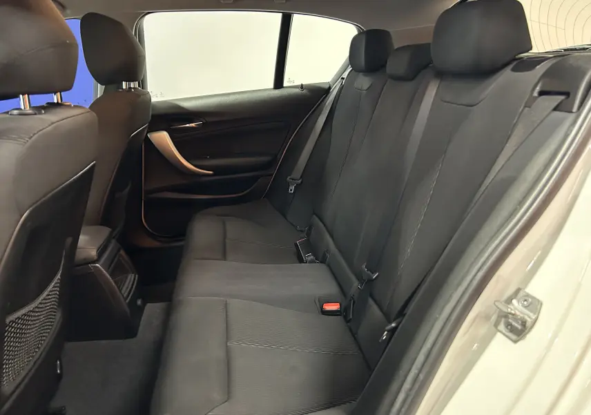Vue intérieure côté droit des sièges arrière noirs d'une BMW Série 1 blanche, montrant les ceintures et les appuie-têtes.