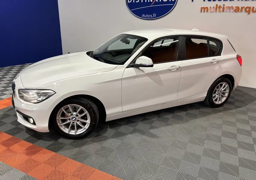 BMW Série 1 116d Business blanche vue en 3/4 avant droit, avec jantes alliage et carrosserie propre en showroom.