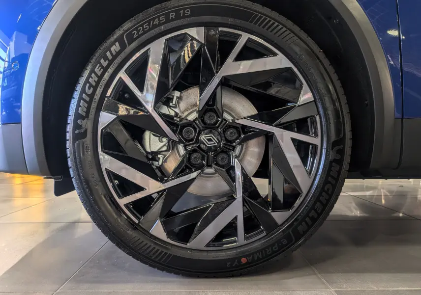 Gros plan sur la roue avant droite du Renault Captur E-TECH bleu Iron avec jante alliage noire et argentée au design géométrique.